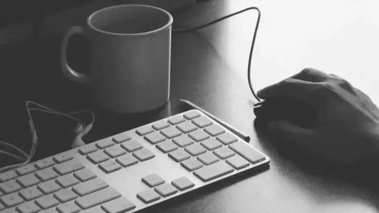 Black an white photo of a keyboard, mouse and coffee cup
