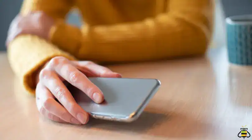 Hand holding a cell phone at a table