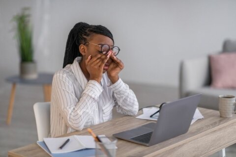 A female rubbing her eyes in frustration sitting at her computer