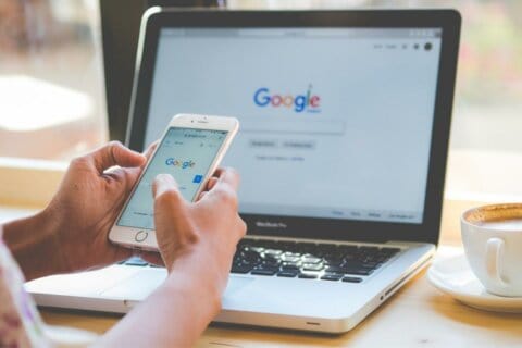 Person holding a phone sitting in front of a laptop